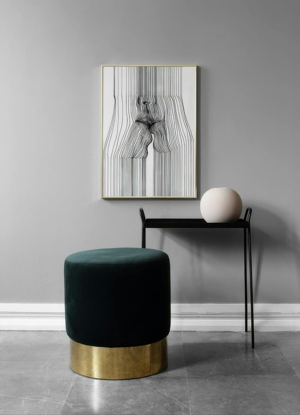 Affiche dun visage fait de lignes noires et blanches, suspendue dans un intérieur gris avec un tabouret vert.