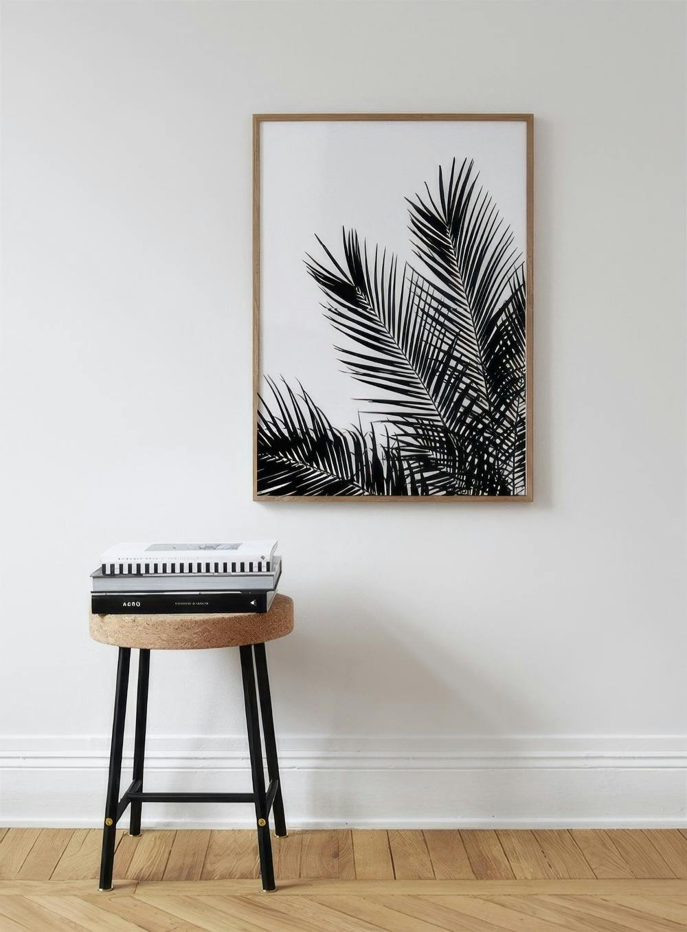 Affiche avec feuilles de palmier noires sur fond blanc, suspendue au-dessus dun tabouret avec des livres.