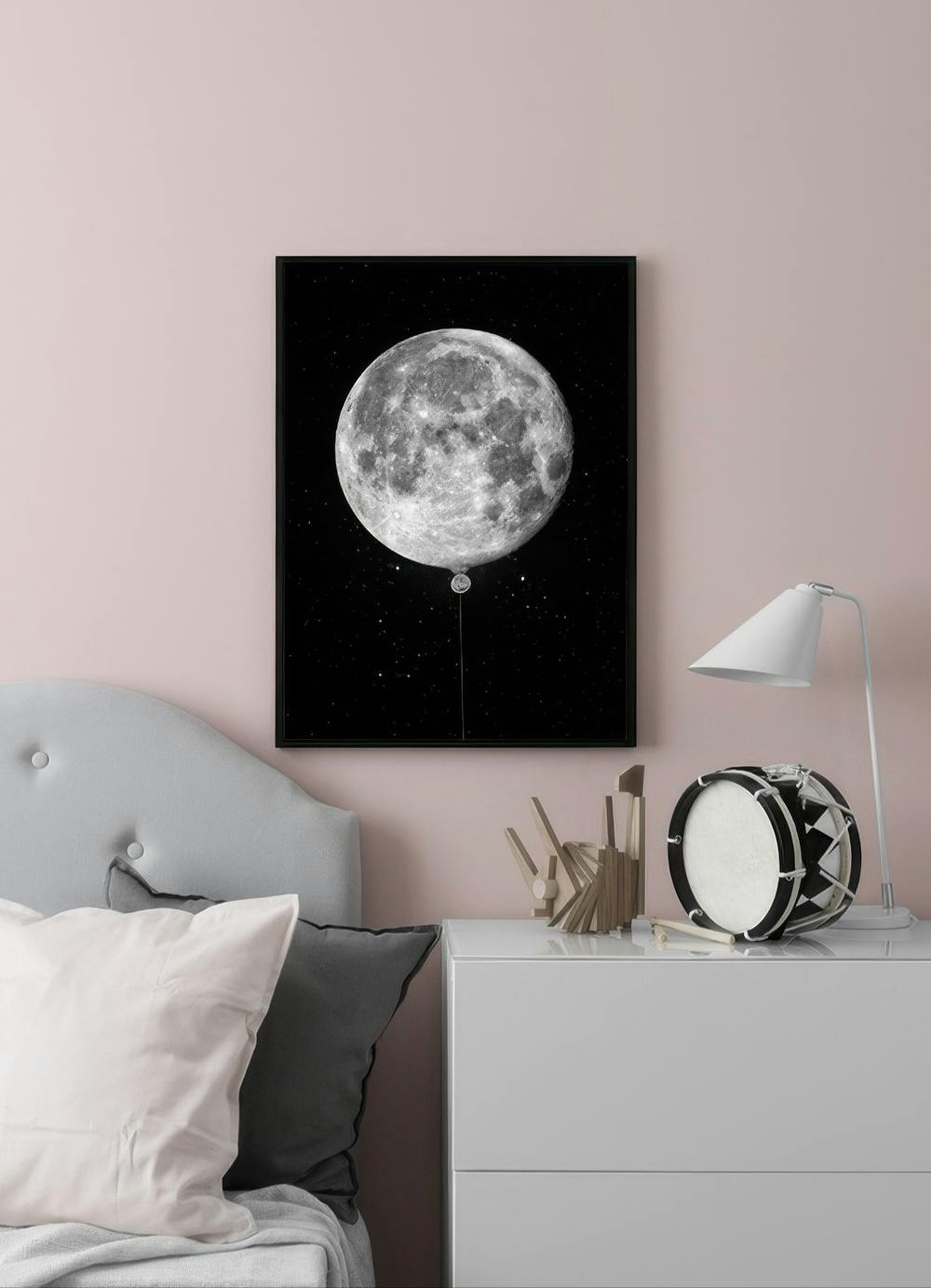 Affiche lune avec un ballon en forme de lune sur fond étoilé, accrochée dans une chambre rose pastel au-dessus dune commode.
