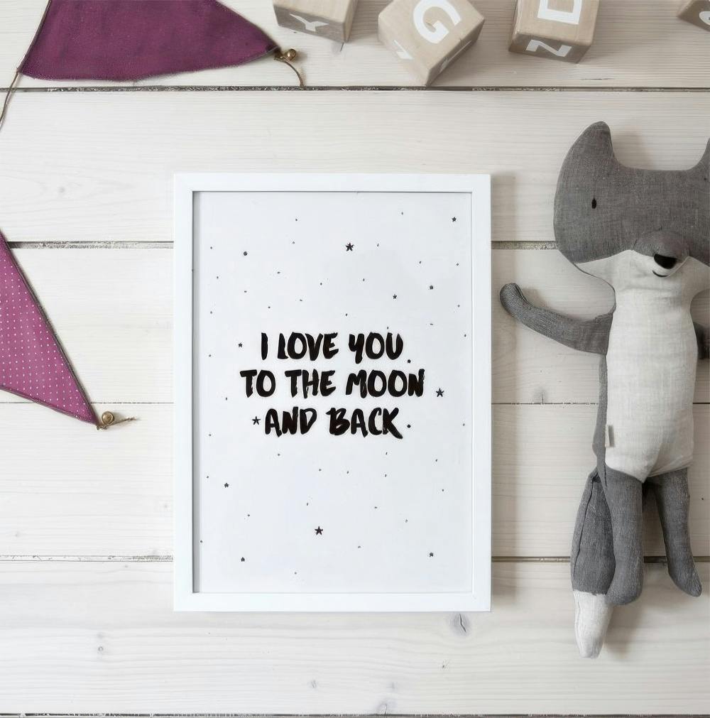 Affiche I LOVE YOU TO THE MOON AND BACK sur une surface en bois clair avec des jouets denfant.