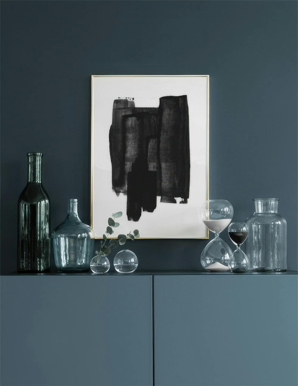 Affiche abstraite noire sur fond blanc, exposée au-dessus dun meuble bleu foncé avec des objets décoratifs.