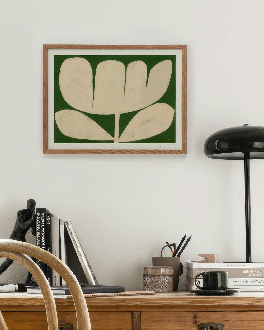 Affiche dune fleur beige aux formes organiques sur fond vert, suspendue au-dessus dun bureau en bois.