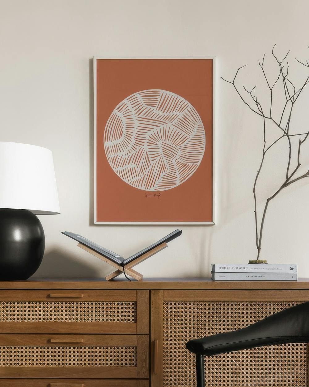 Affiche terracotta avec des motifs abstraits circulaires blancs, accrochée au-dessus dune commode en rotin.
