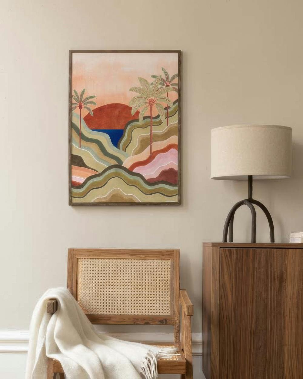 Affiche de paysage tropical stylisé avec palmiers, soleil et collines colorées, sur un mur beige dans un salon.