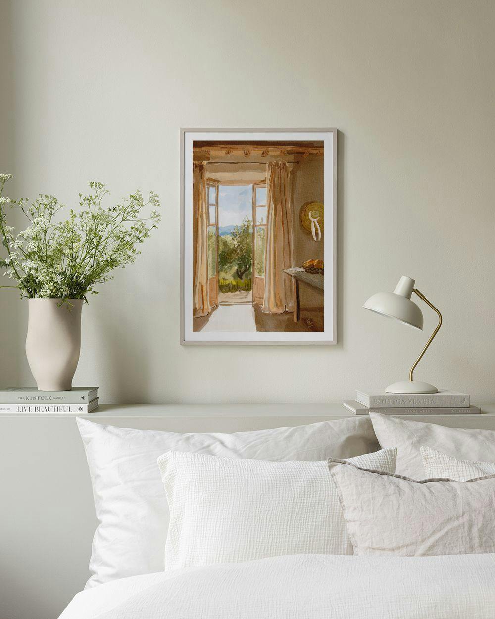 Affiche dune vue sur un paysage méditerranéen depuis une pièce, suspendue au-dessus dun lit avec oreillers blancs.