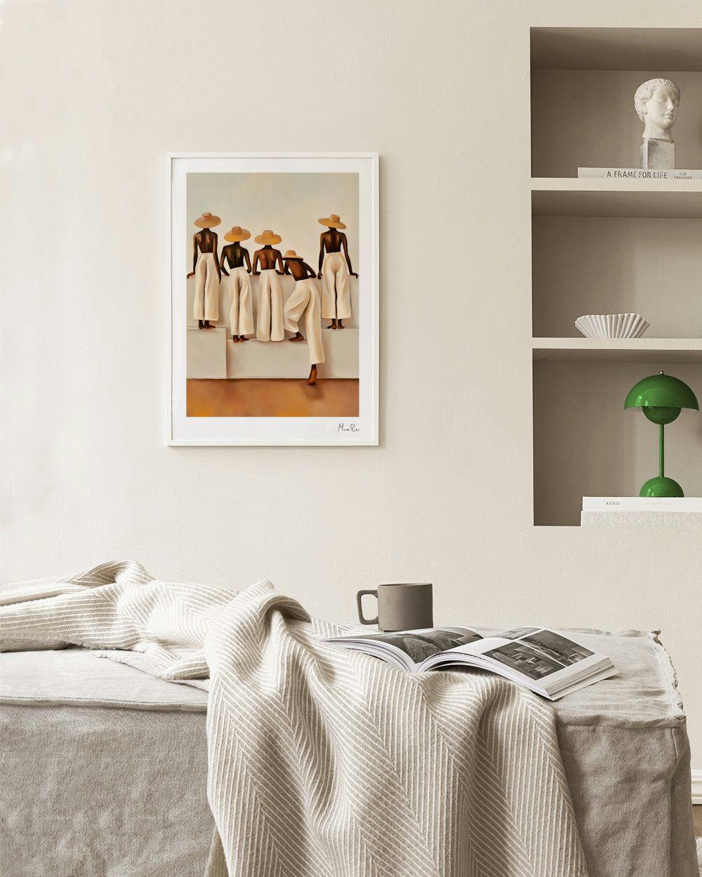 Affiche avec des femmes aux larges chapeaux et pantalons clairs, accrochée dans un salon moderne au-dessus dun banc.