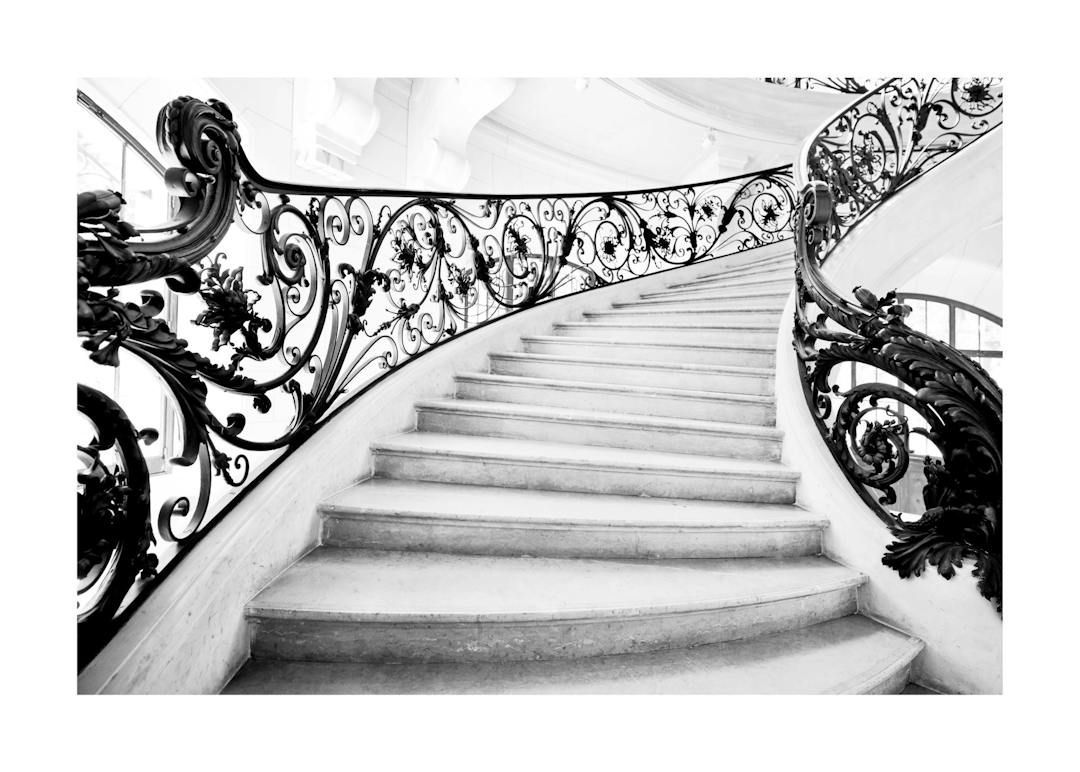 Affiche noir et blanc dun escalier Art Nouveau avec une rampe en fer forgé aux motifs floraux et volutes.