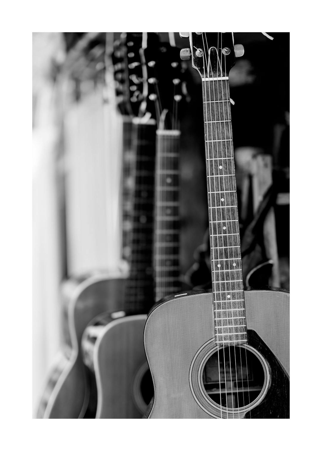 Affiche noir et blanc avec une rangée de guitares acoustiques, la première au premier plan mettant en valeur son manche et ses c