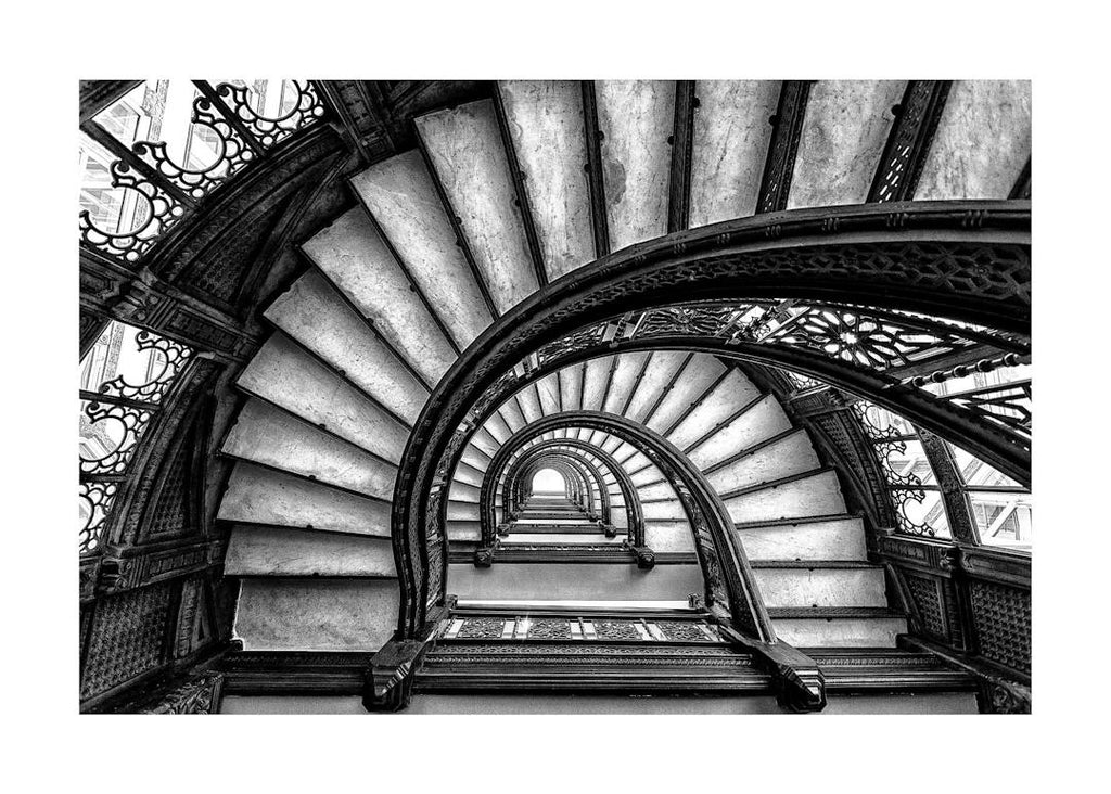 Affiche noir et blanc avec une vue en plongée dun escalier en colimaçon orné de rampes en fer forgé, créant une spirale vers le 