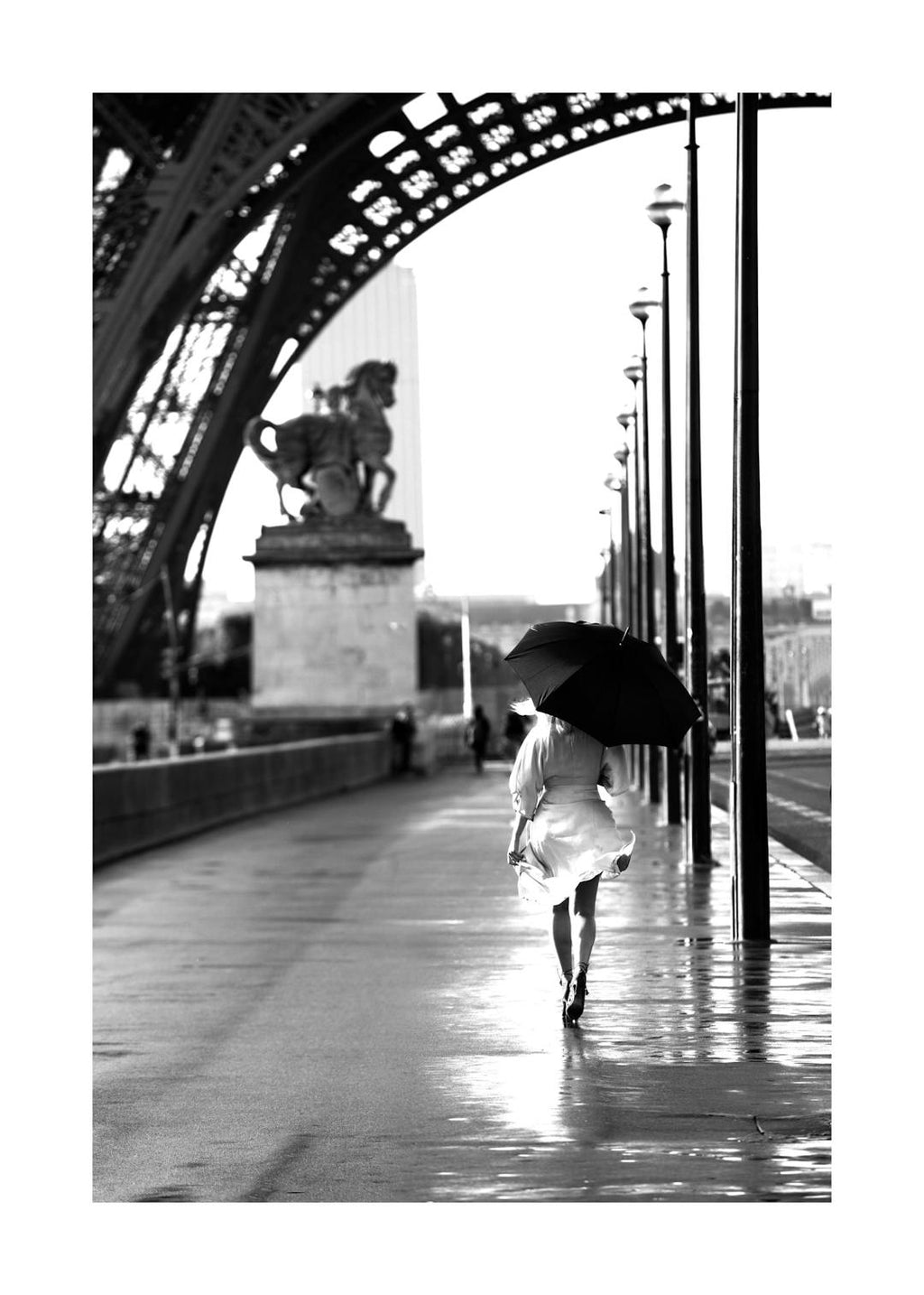 Affiche noir et blanc, femme avec parapluie marchant sous la Tour Eiffel à Paris, typographie élégante.