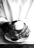 Affiche noir et blanc dune tasse de café au lait mousseux tenue par des mains, avec une cuillère sur une soucoupe au St Regis à 