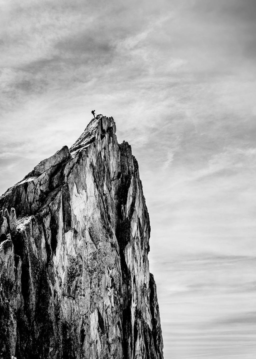 Affiche noir et blanc dun alpiniste au sommet dune montagne rocheuse, sur fond de ciel nuageux