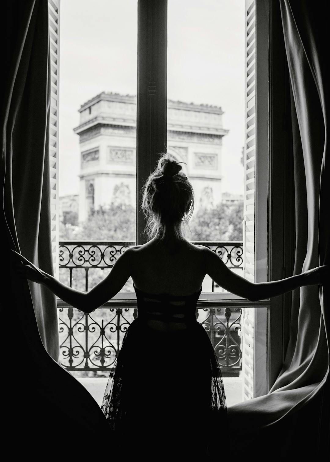 Affiche noir et blanc femme regardant lArc de Triomphe de Paris depuis une fenêtre avec des rideaux ouverts, style photographie