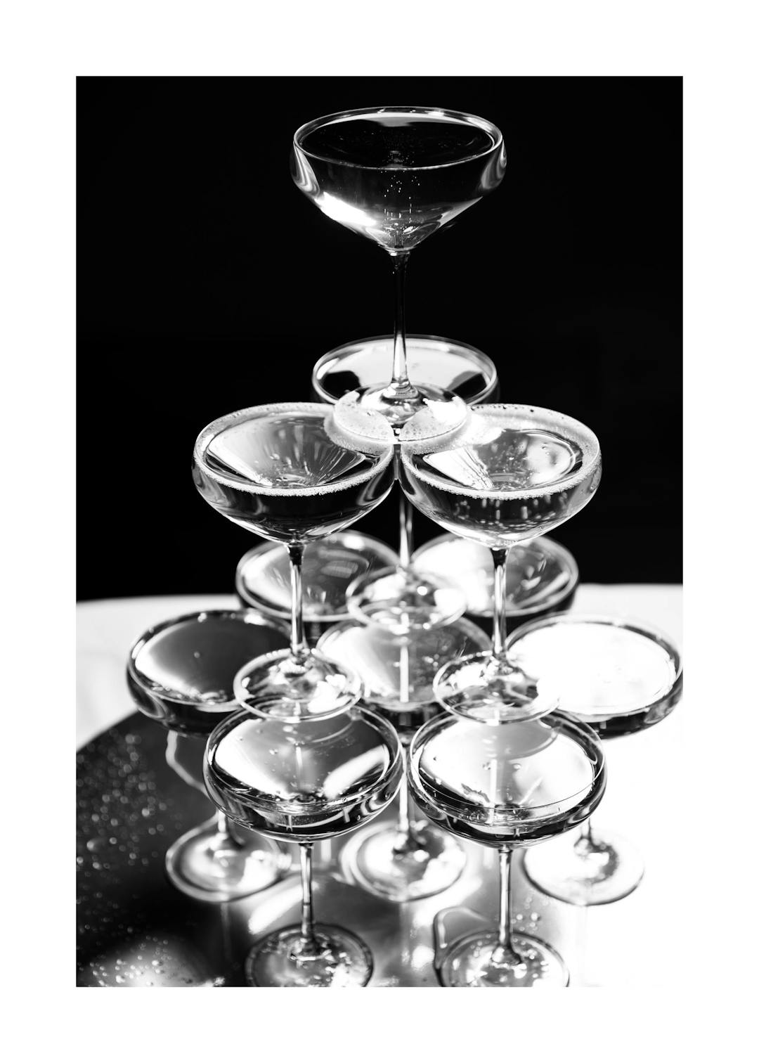 Affiche noir et blanc dune pyramide de coupes de champagne, avec bulles et reflets lumineux. Typographie élégante.