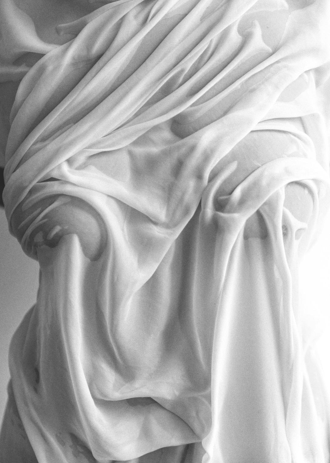Affiche noir et blanc dun tissu fluide, drapé sur un corps, révélant des formes subtiles par transparence et reflets lumineux.