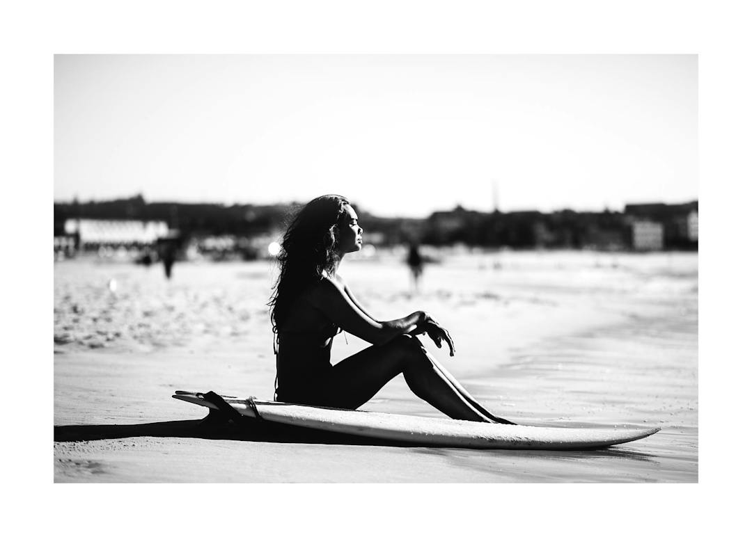 Affiche noir et blanc dune femme assise sur sa planche de surf sur une plage
