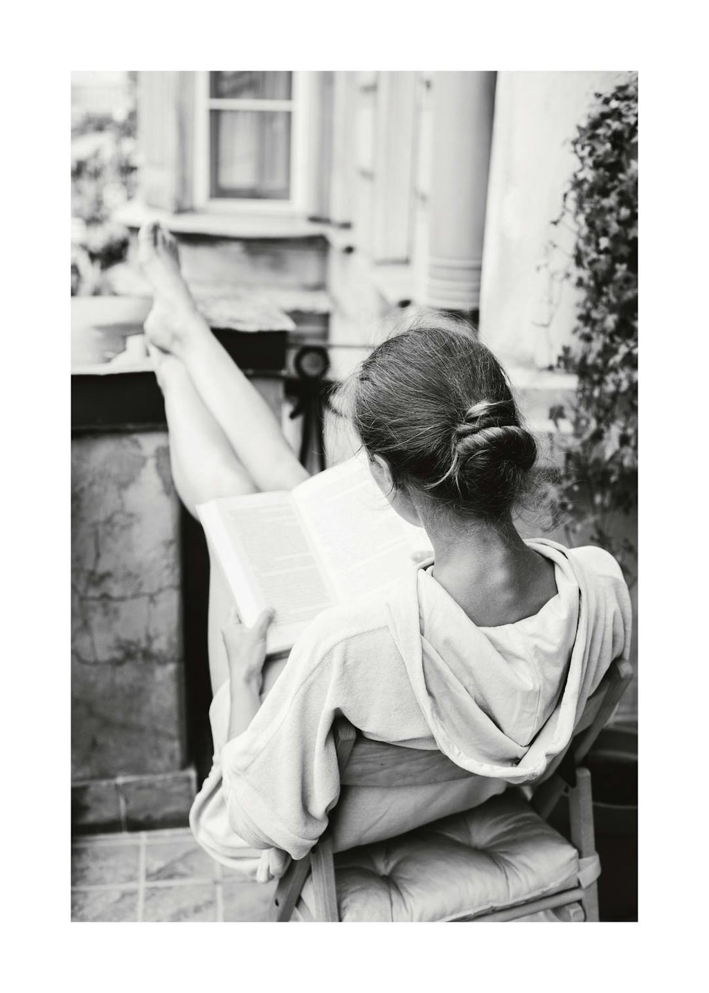 Affiche noir et blanc de femme lisant un livre, jambes levées, assise sur une chaise. Photographie de détente.