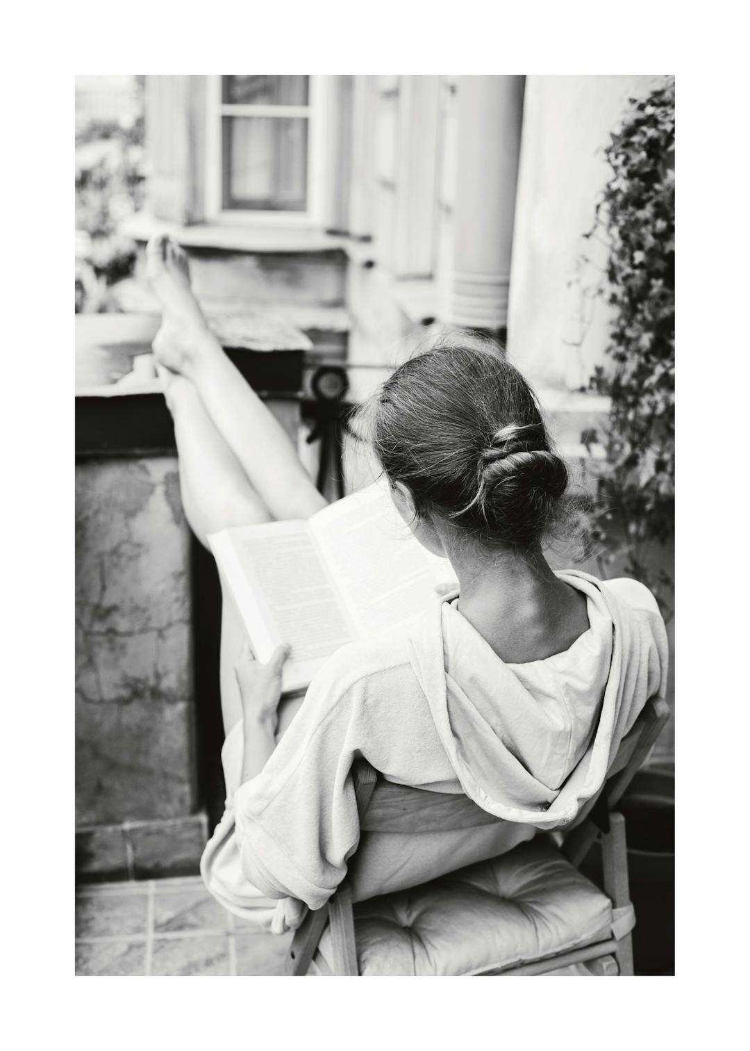 Affiche noir et blanc de femme lisant un livre, jambes levées, assise sur une chaise. Photographie de détente.