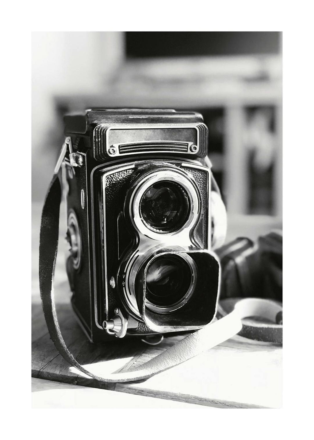 Affiche en noir et blanc dun appareil photo rétro vintage avec sa sangle en cuir sur une surface en bois