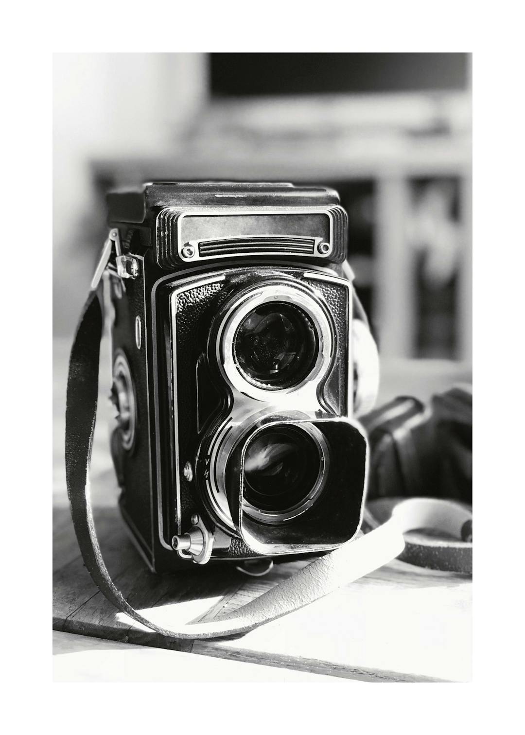 Affiche en noir et blanc dun appareil photo rétro vintage avec sa sangle en cuir sur une surface en bois