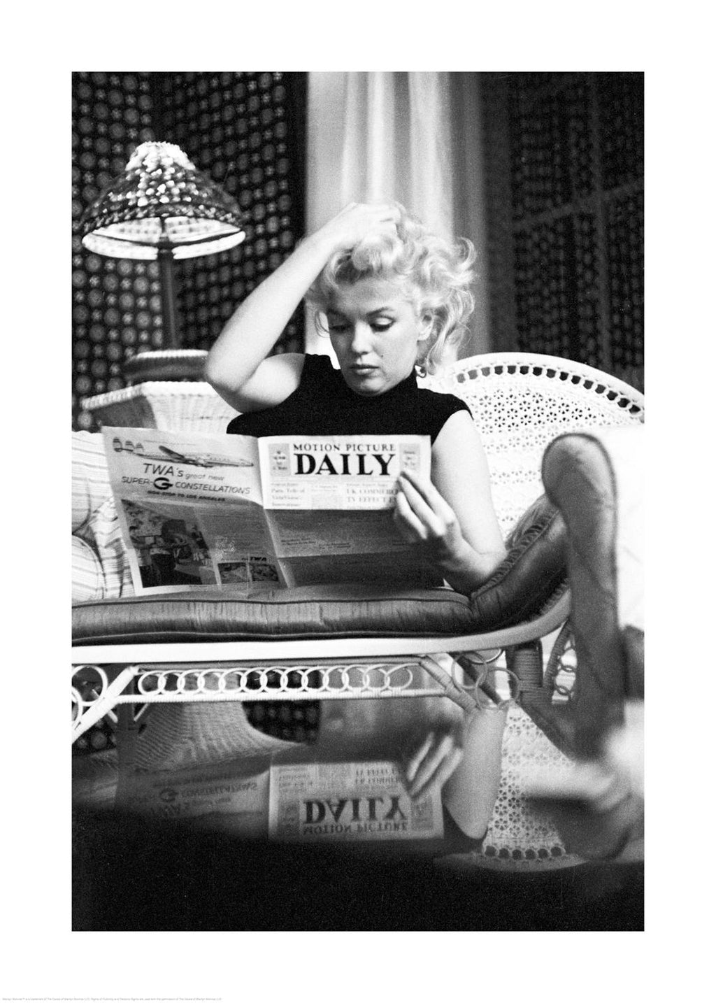 Affiche noir et blanc de Marilyn Monroe lisant un journal sur un canapé, cheveux blonds décoiffés et regard concentré.