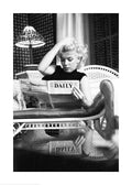 Affiche noir et blanc de Marilyn Monroe lisant un journal sur un canapé, cheveux blonds décoiffés et regard concentré.