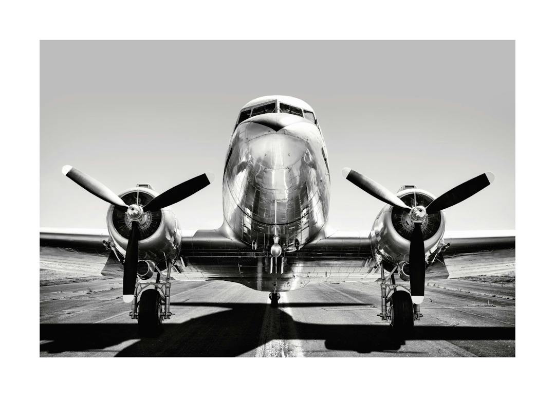 Affiche noir et blanc dun avion vintage, vue de face, avec un fuselage métallique brillant et des hélices détaillées.