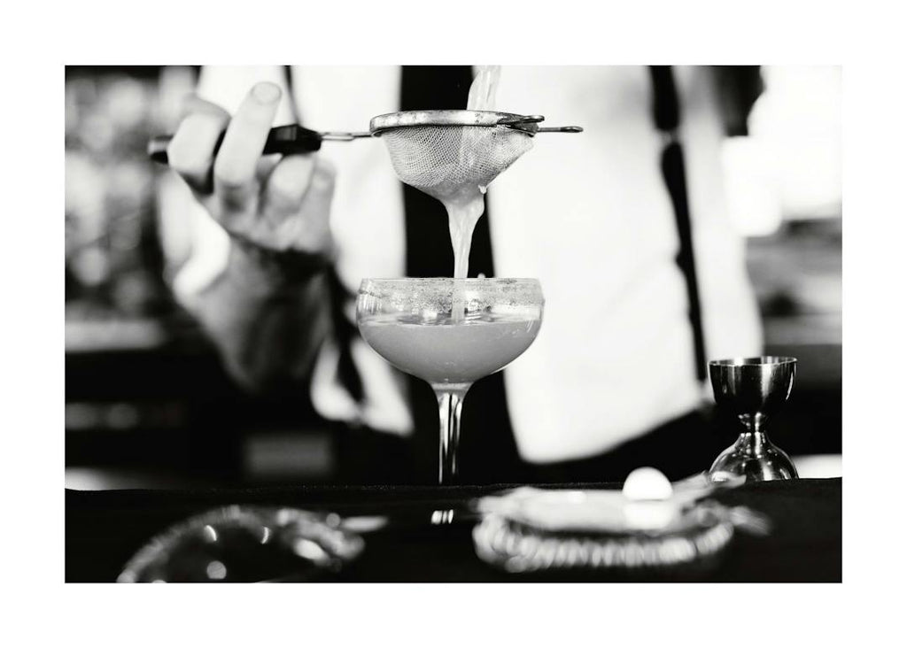 Affiche noir et blanc dun barman filtrant un cocktail dans un verre, ambiance mixologie