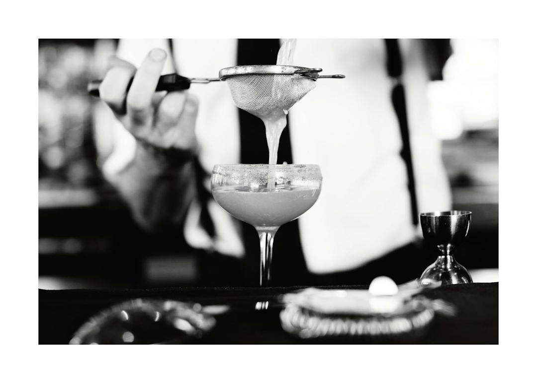 Affiche noir et blanc dun barman filtrant un cocktail dans un verre, ambiance mixologie