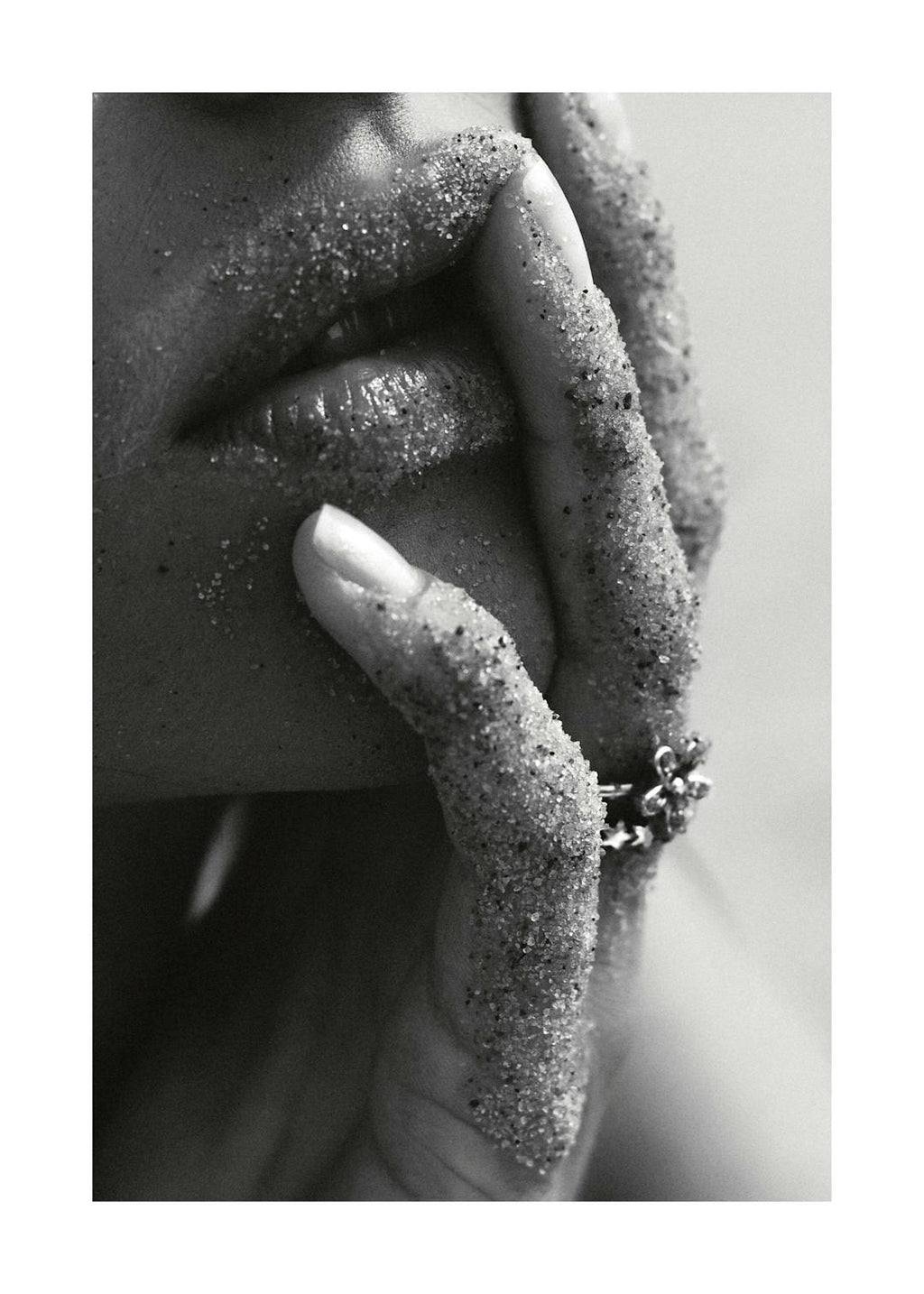 Affiche noir et blanc. Gros plan sur les lèvres et les doigts dune femme recouverts de sable, avec une bague fleur.