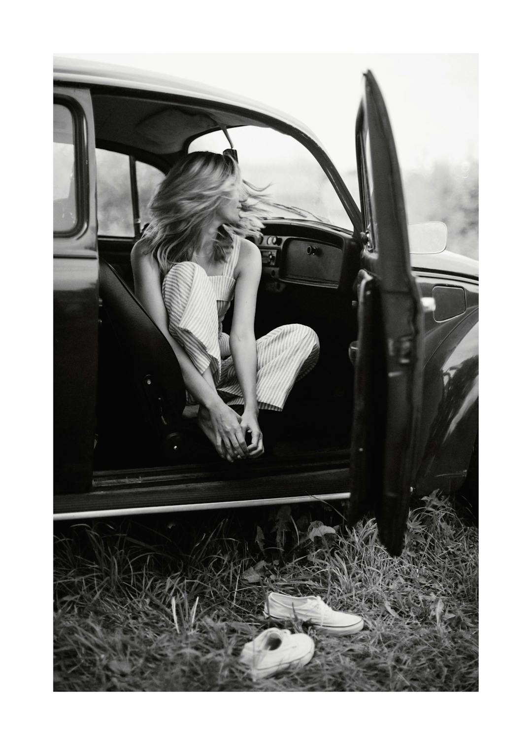 Affiche noir et blanc, femme assise dans une voiture ancienne, portière ouverte, chaussures dans lherbe