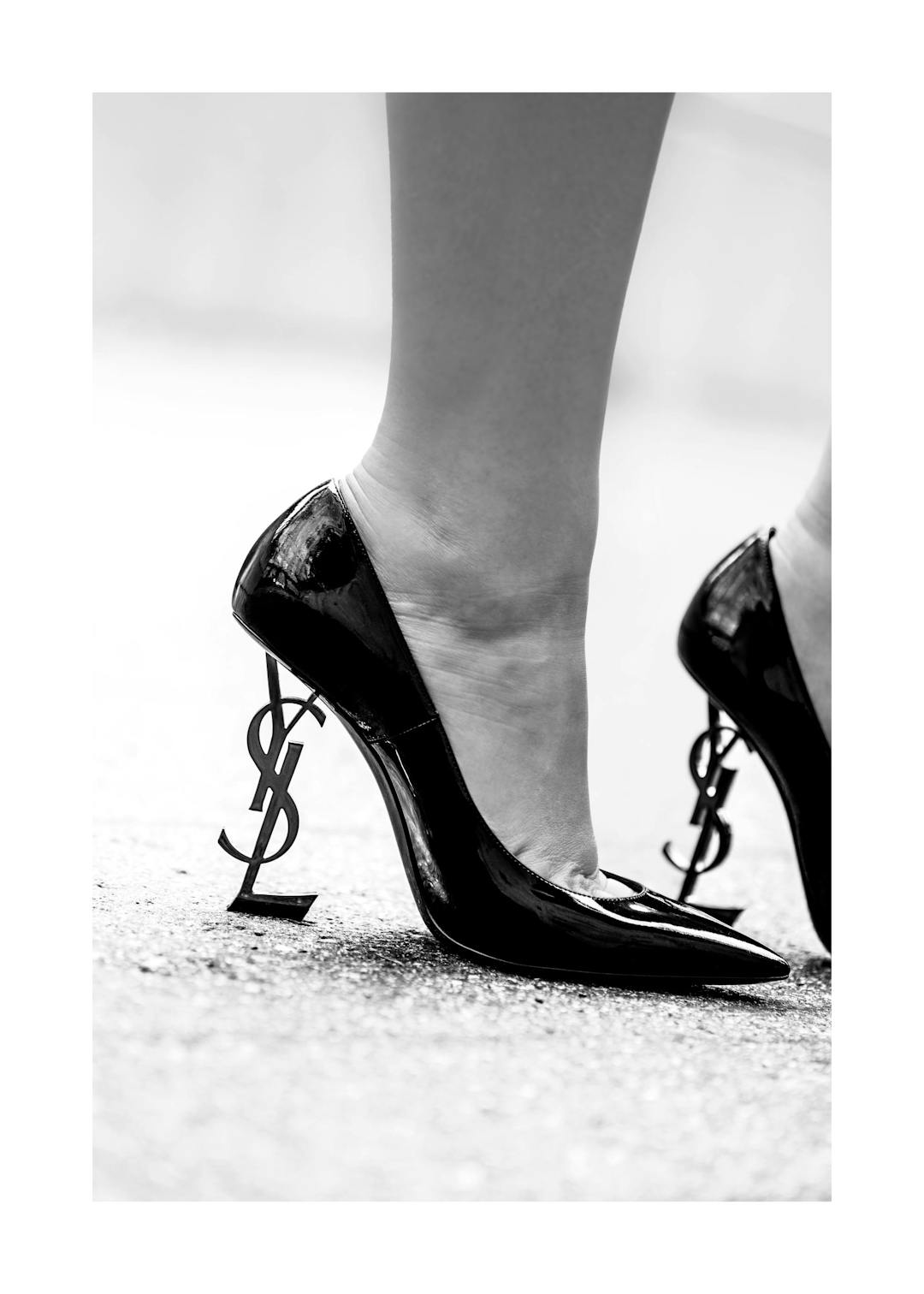 Affiche en noir et blanc dun pied féminin chaussé dun talon aiguille noir YSL avec le logo en guise de talon