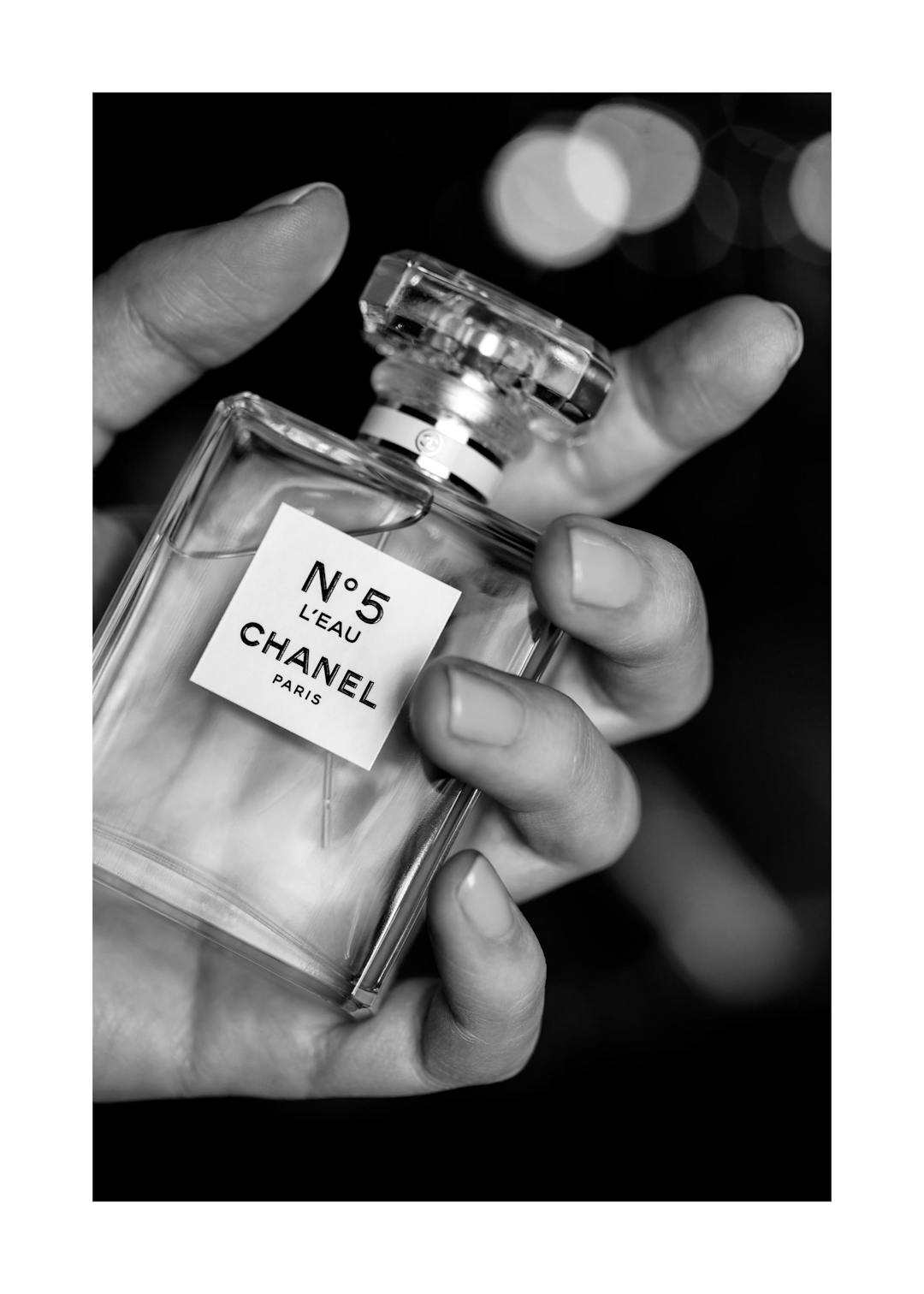 Affiche en noir et blanc dune main tenant un flacon de parfum Chanel N°5, typographie sur létiquette