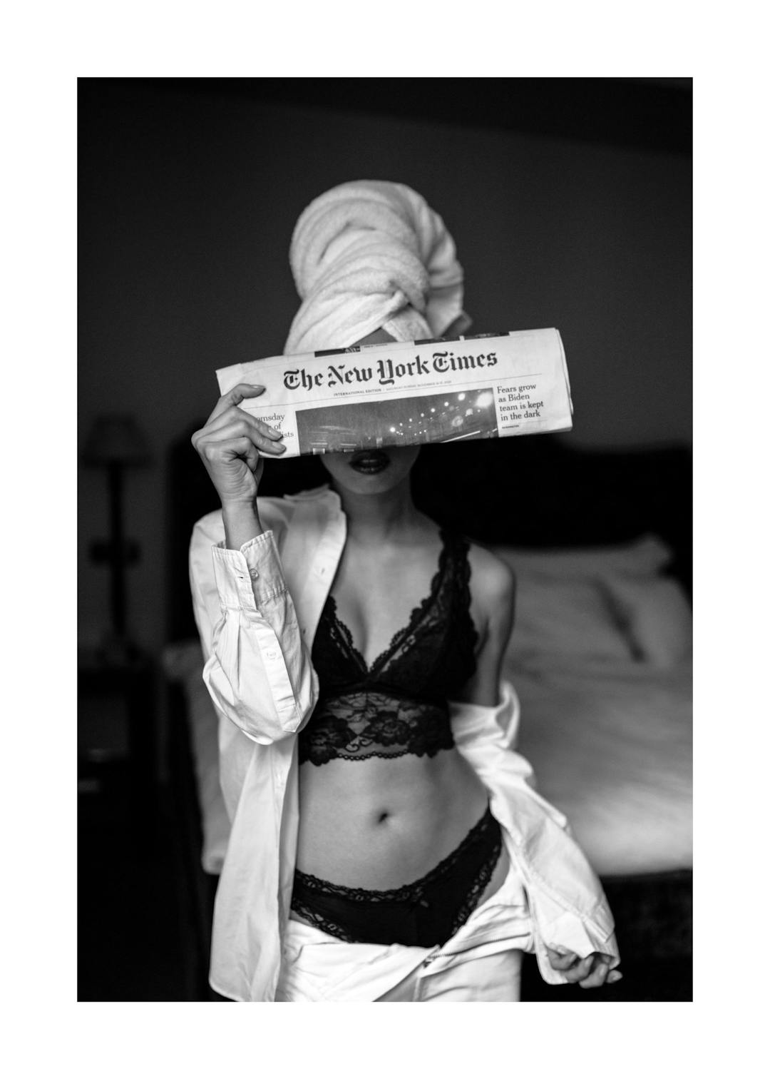 Affiche noir et blanc dune femme en lingerie et pyjama, les cheveux dans une serviette, lisant le journal