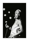 Affiche noir et blanc de Nina Simone tenant un micro, avec un foulard et des boucles doreilles, sur scène.