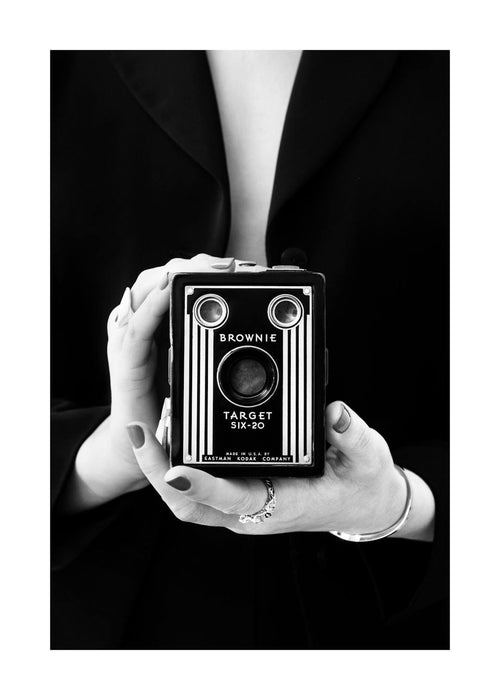 Affiche de photographie en noir et blanc dune femme tenant un appareil photo rétro devant son corps, avec le mot Brownie.