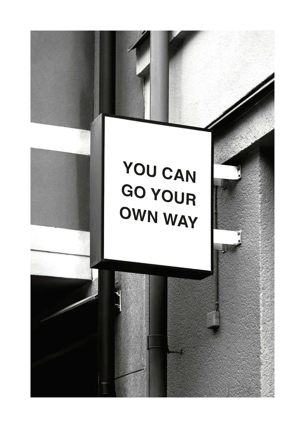 Affiche noir et blanc dun panneau carré avec le texte You can go your own way sur un mur dhabitation