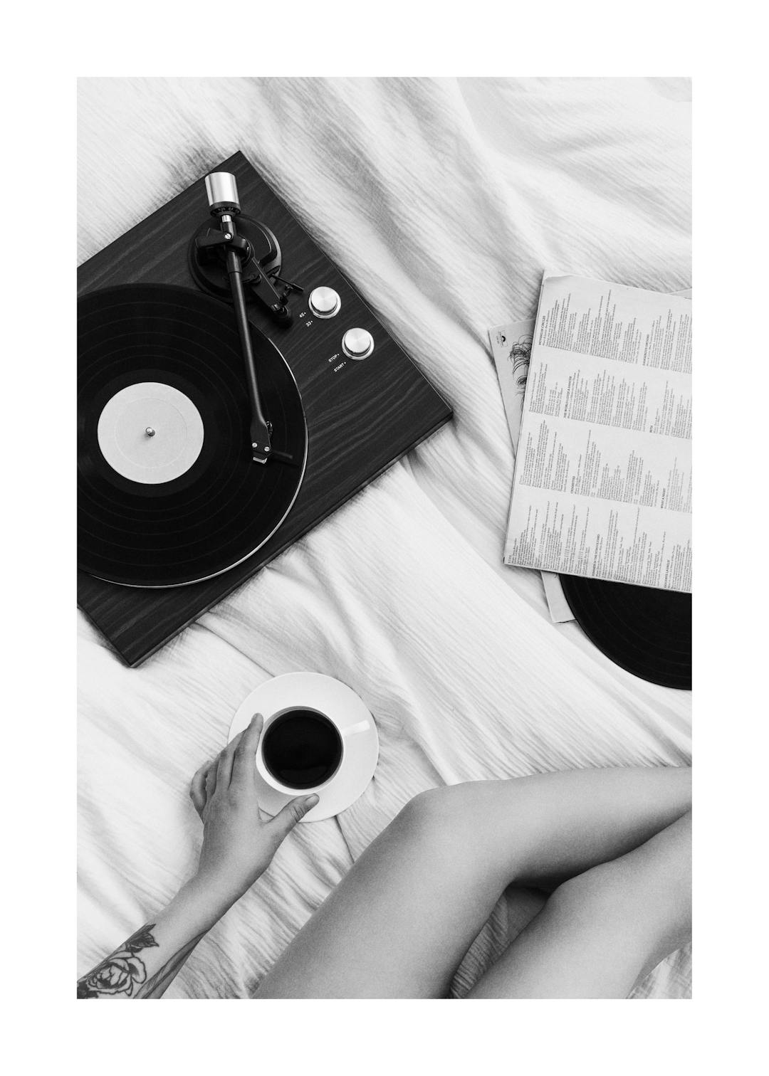 Affiche noir et blanc dune personne écoutant un disque vinyle avec une tasse de café sur un lit.