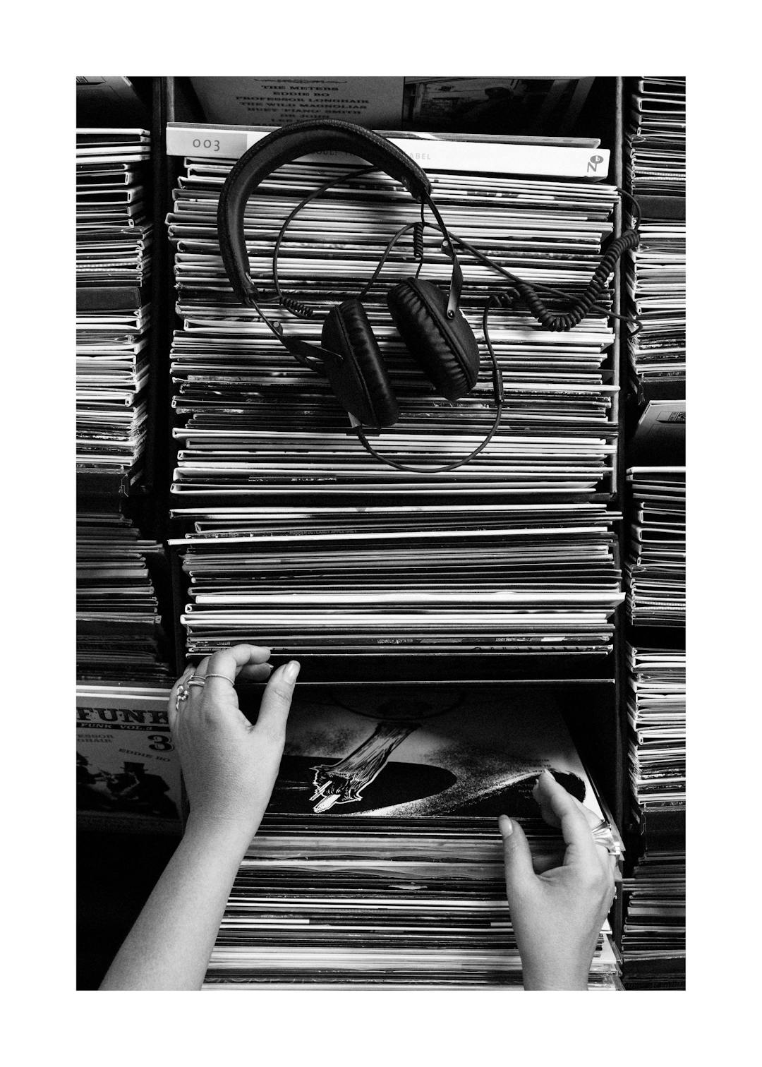 Affiche monochrome dune femme cherchant un disque vinyle dans une archive, avec un casque posé sur des disques, musique nostalgi