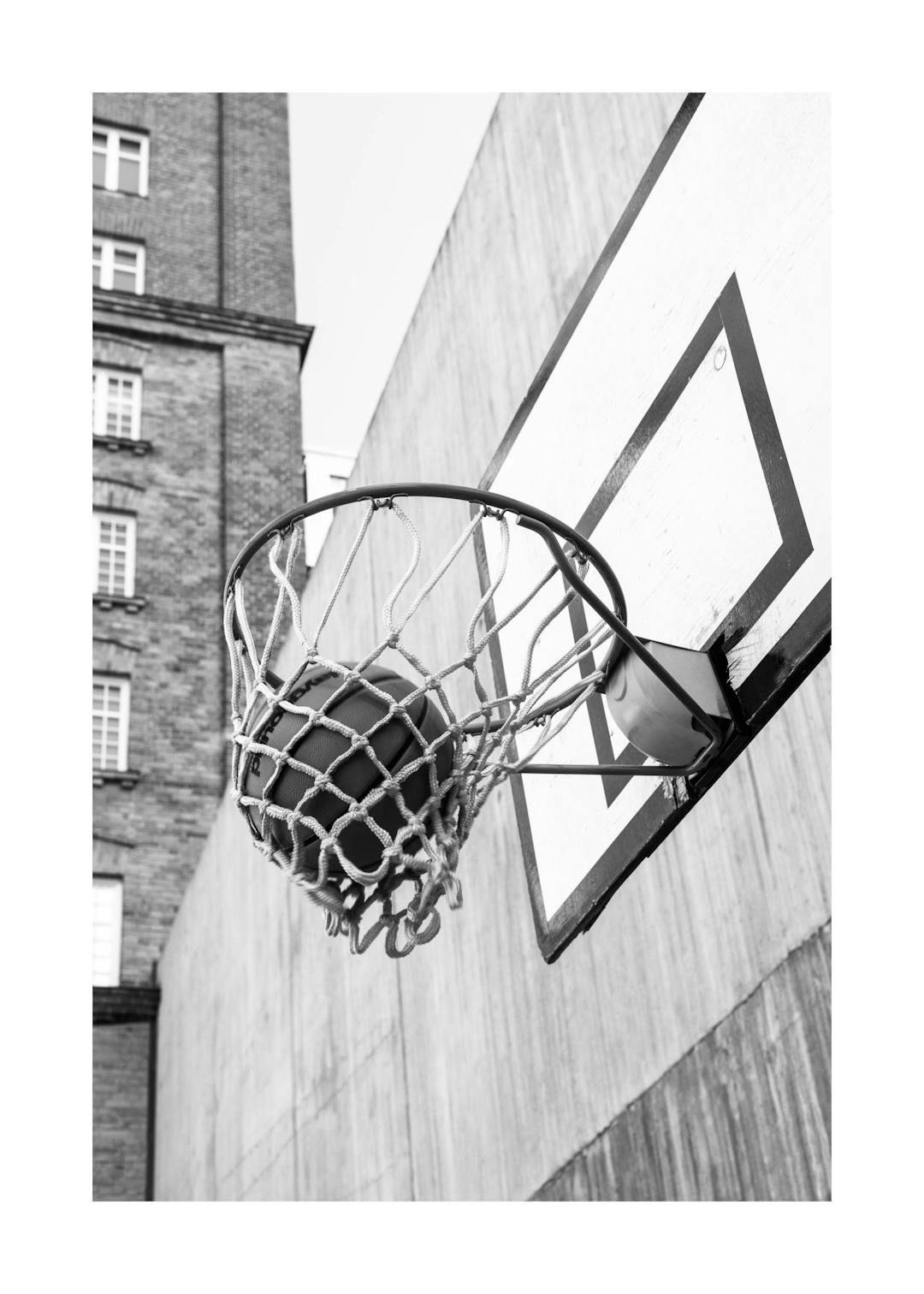 Affiche noir et blanc dun panier de basketball avec un ballon dedans, sur un terrain de sport urbain