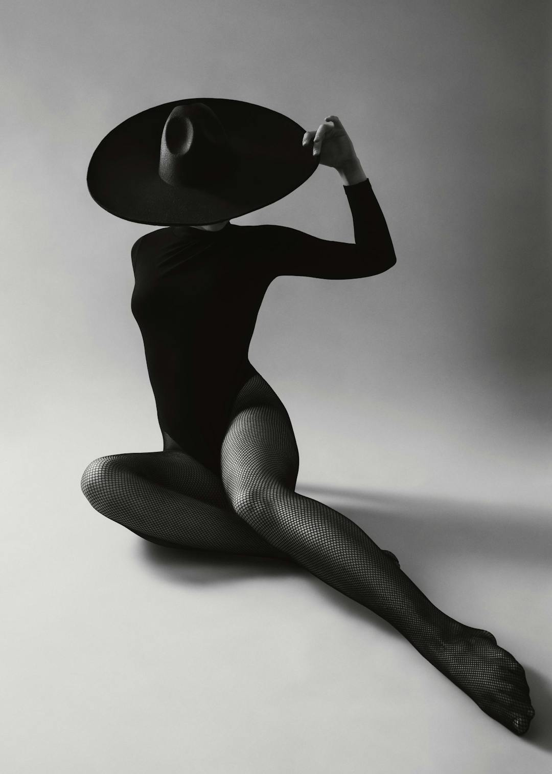 Affiche monochrome dune femme audacieuse en justaucorps et bas résille, un grand chapeau cachant son visage