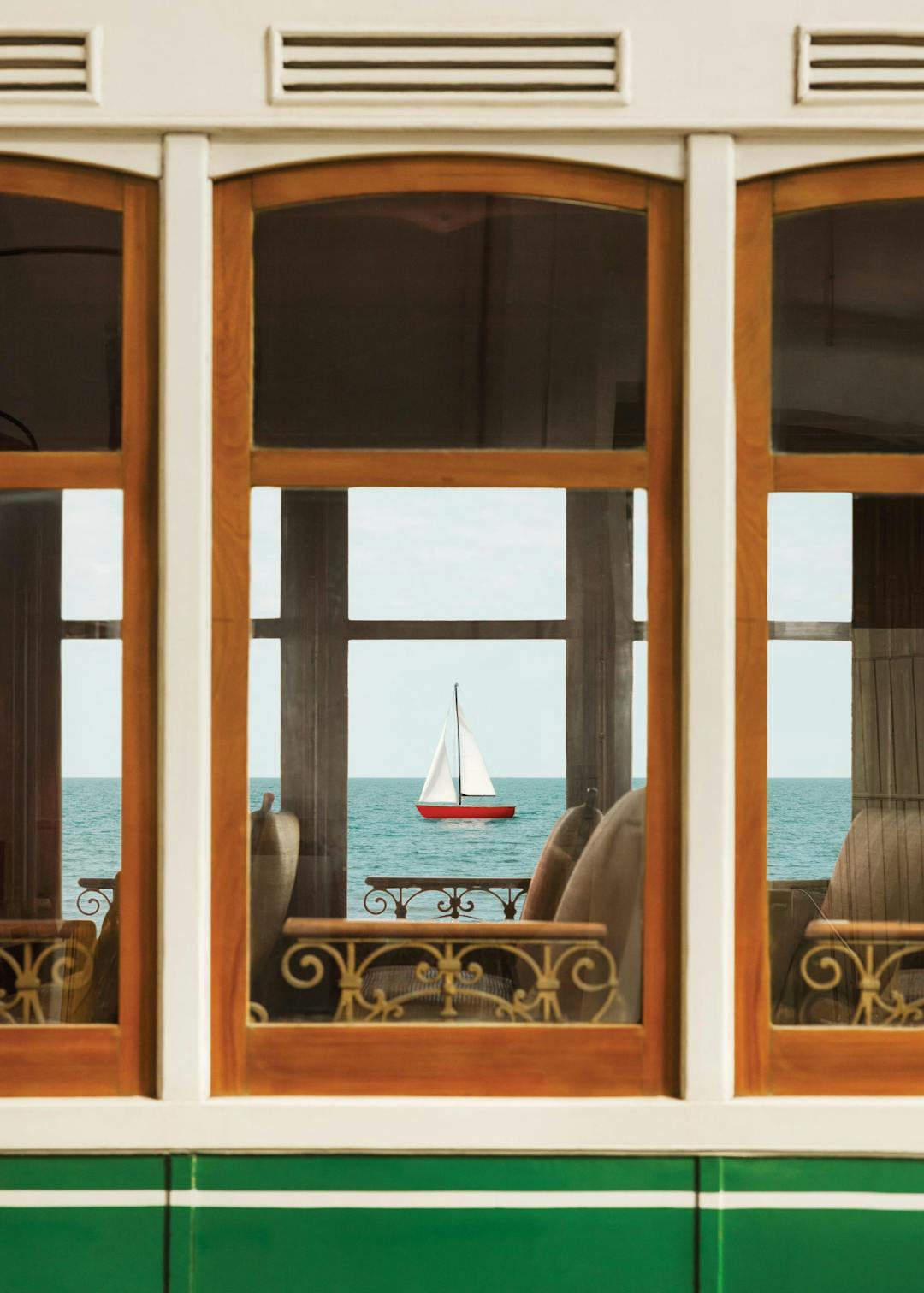 Affiche dun voilier rouge et blanc sur la mer, vu à travers les fenêtres en bois dun tramway vert.