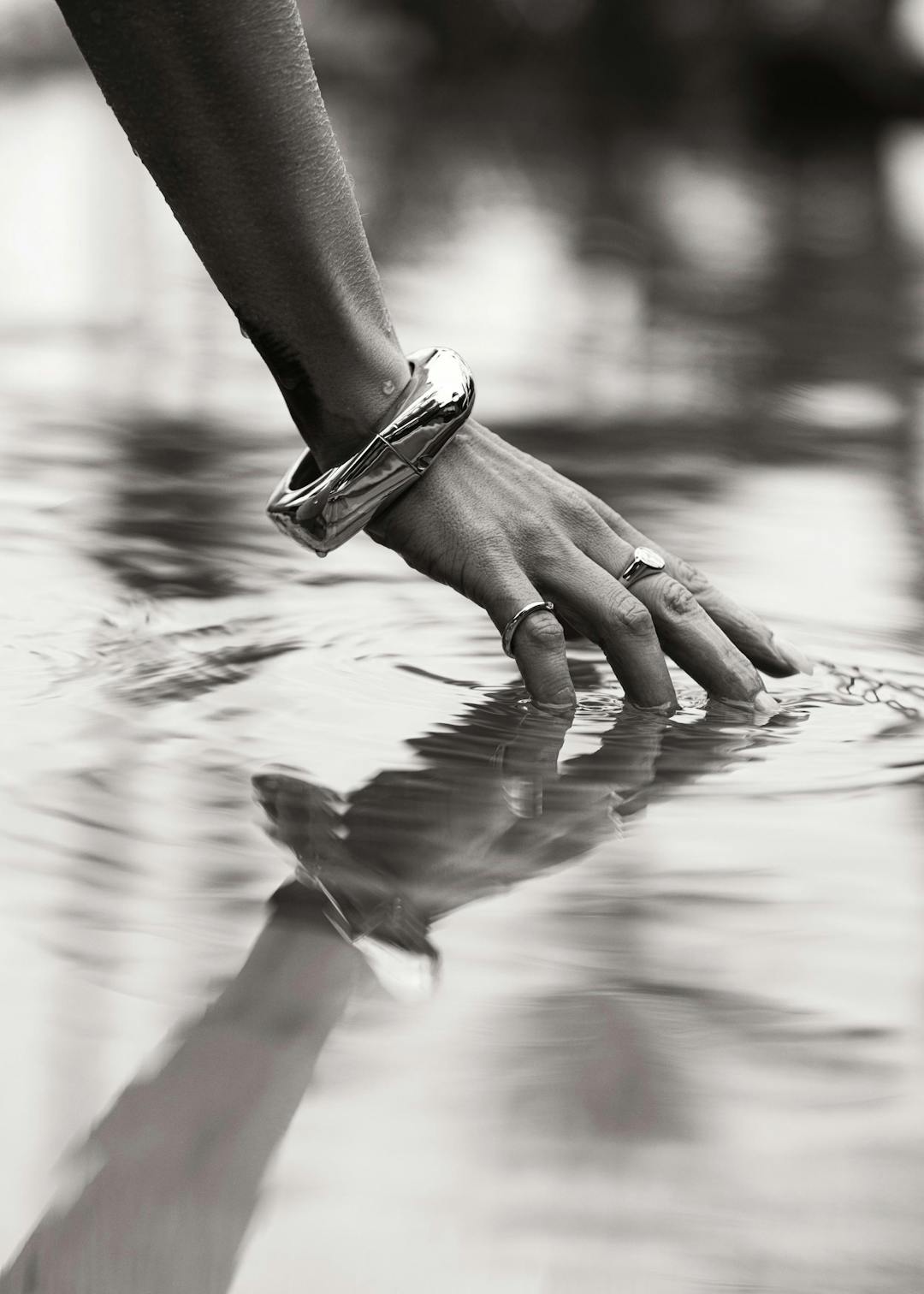 Affiche en noir et blanc dune main avec un bracelet et des bagues, effleurant la surface de leau.