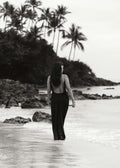 Affiche en noir et blanc dune femme en robe longue marchant sur une plage tropicale avec des palmiers.