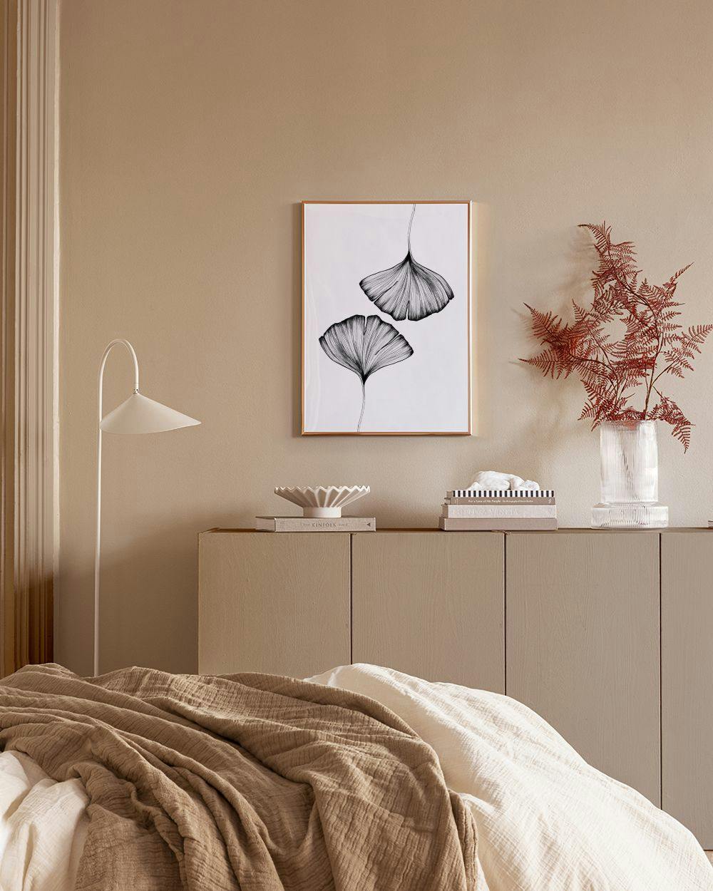 Une affiche de feuilles de ginkgo art linéaire noir et blanc, accrochée sur un mur bleu marine avec motifs géométriques dorés, a