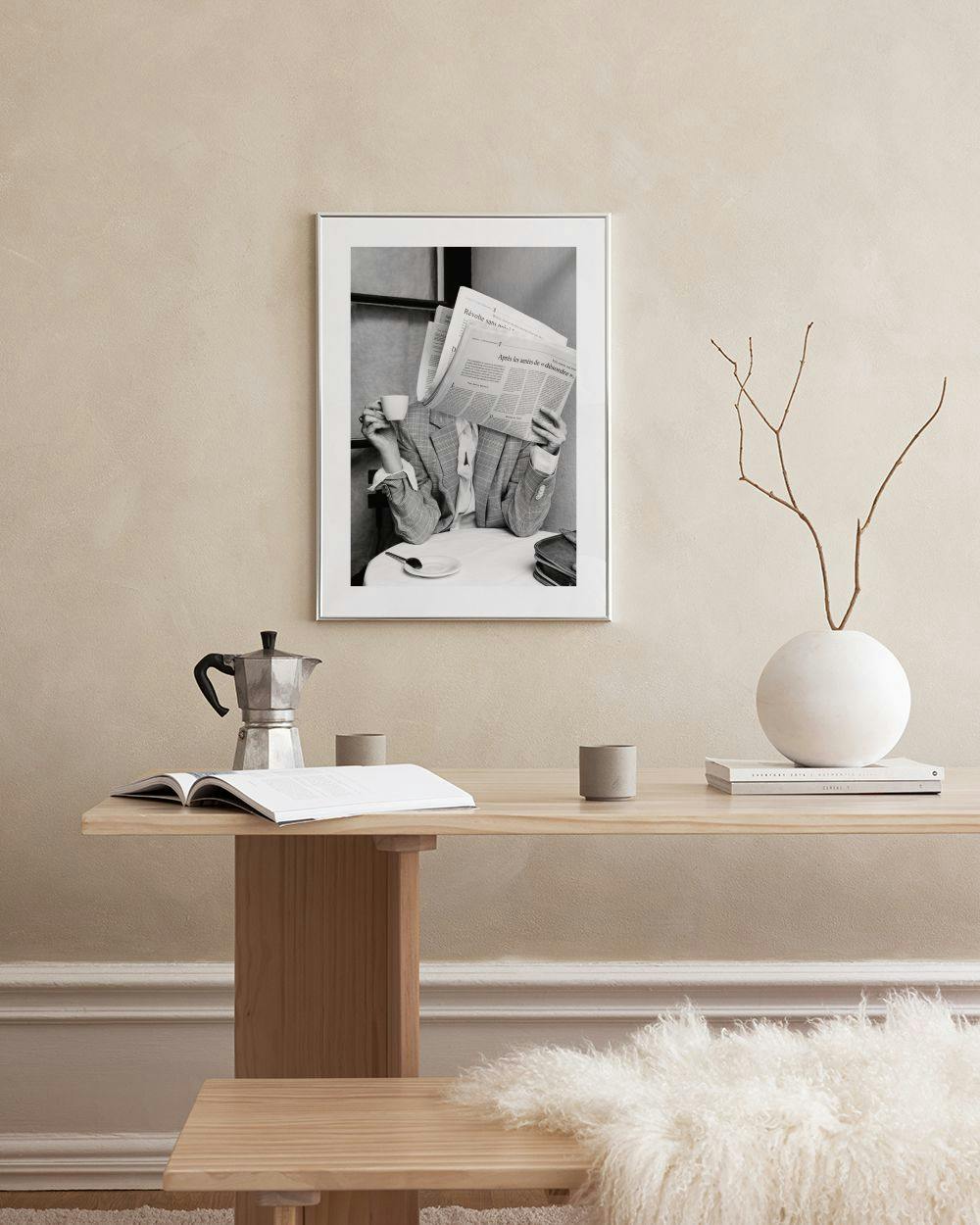 Affiche noir et blanc dune personne lisant un journal et buvant du café, posée sur une console grise.