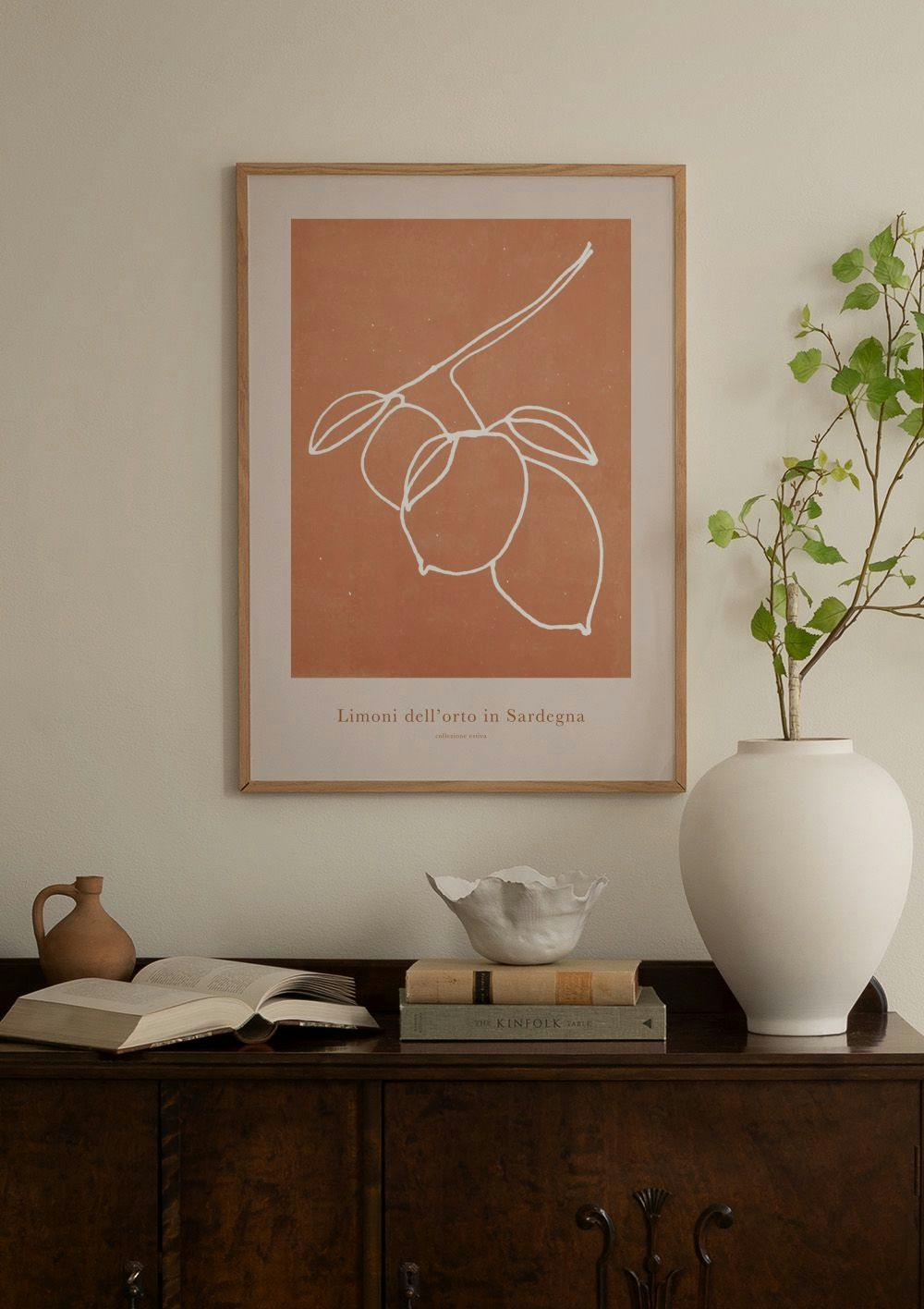 Affiche avec un dessin minimaliste de citrons sur fond terracotta, suspendue au-dessus dun buffet blanc avec des vases décoratif