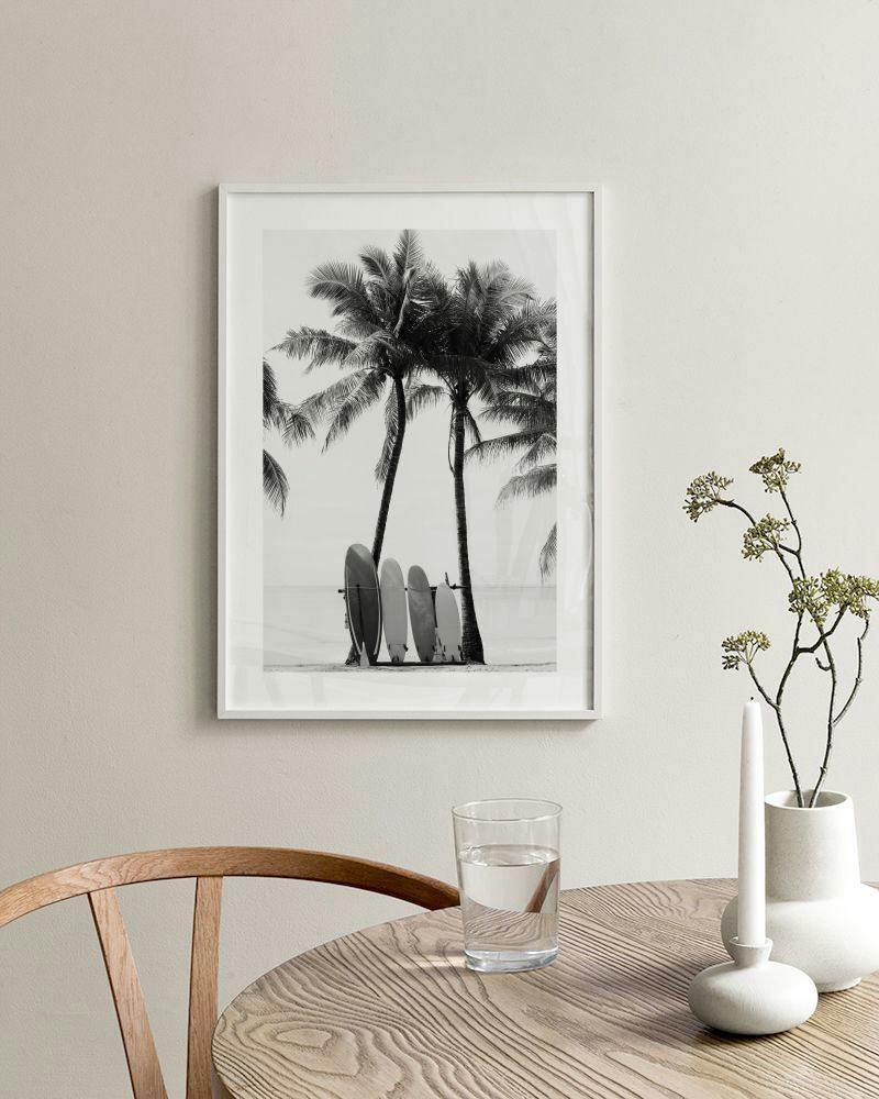 Affiche noir et blanc de palmiers et planches de surf sur une plage, accrochée dans un salon moderne.