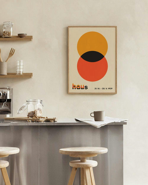 Affiche haus avec deux cercles superposés, orange et rouge, et une forme noire, au-dessus dune étagère noire.