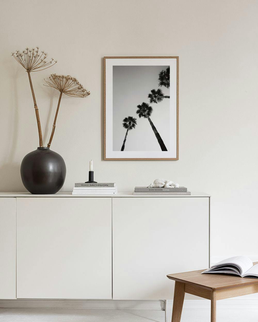 Affiche noir et blanc de palmiers contrastés sur fond clair, accrochée au-dessus dun buffet moderne.